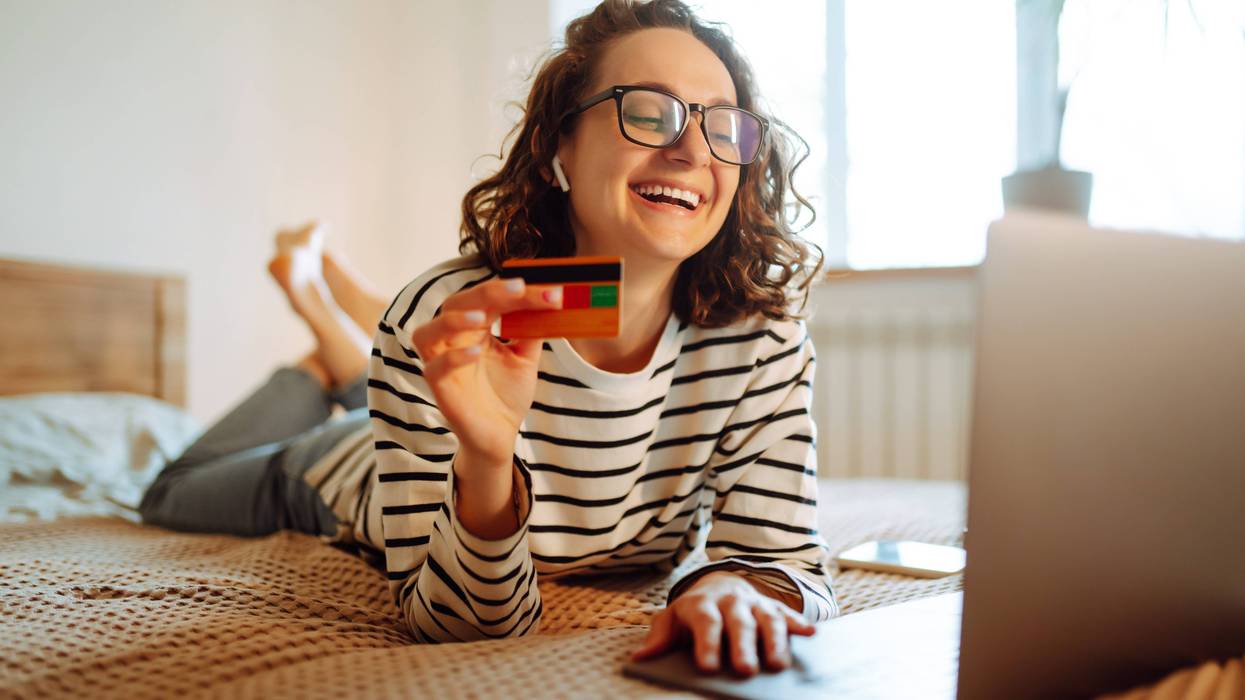 Online shopping аt home. A young woman holds a credit card and uses a laptop. Black friday, sale, consumerist, lifestyle concept.