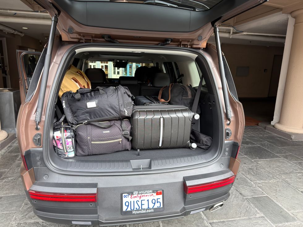 Open brown SUV trunk packed full of suitcases and duffel bags.