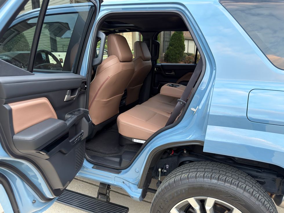 Open rear door of a light blue SUV, showing brown and black interior with rear seats.