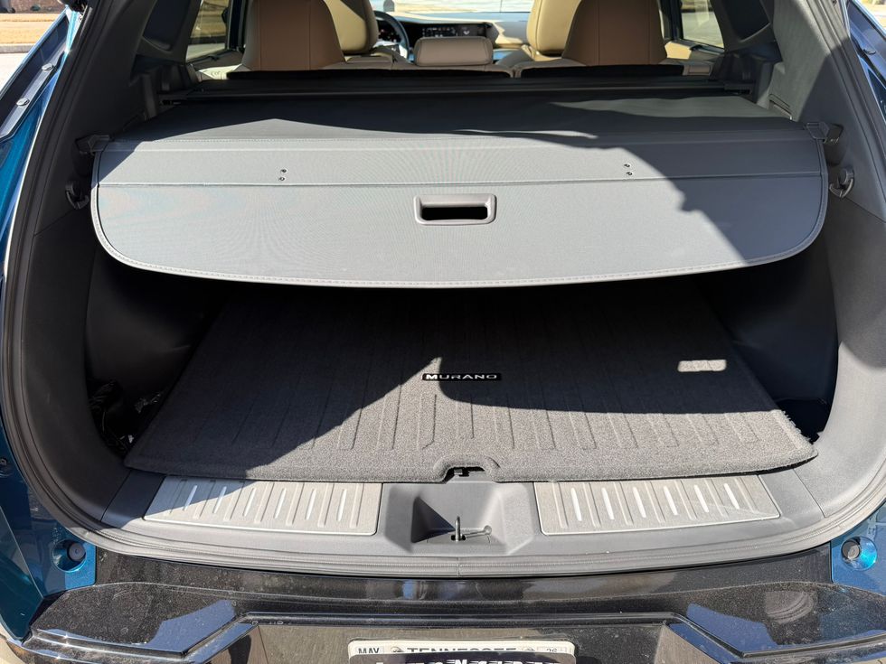 Open trunk of a Nissan Murano SUV with an extended grey cargo cover and floor mat.
