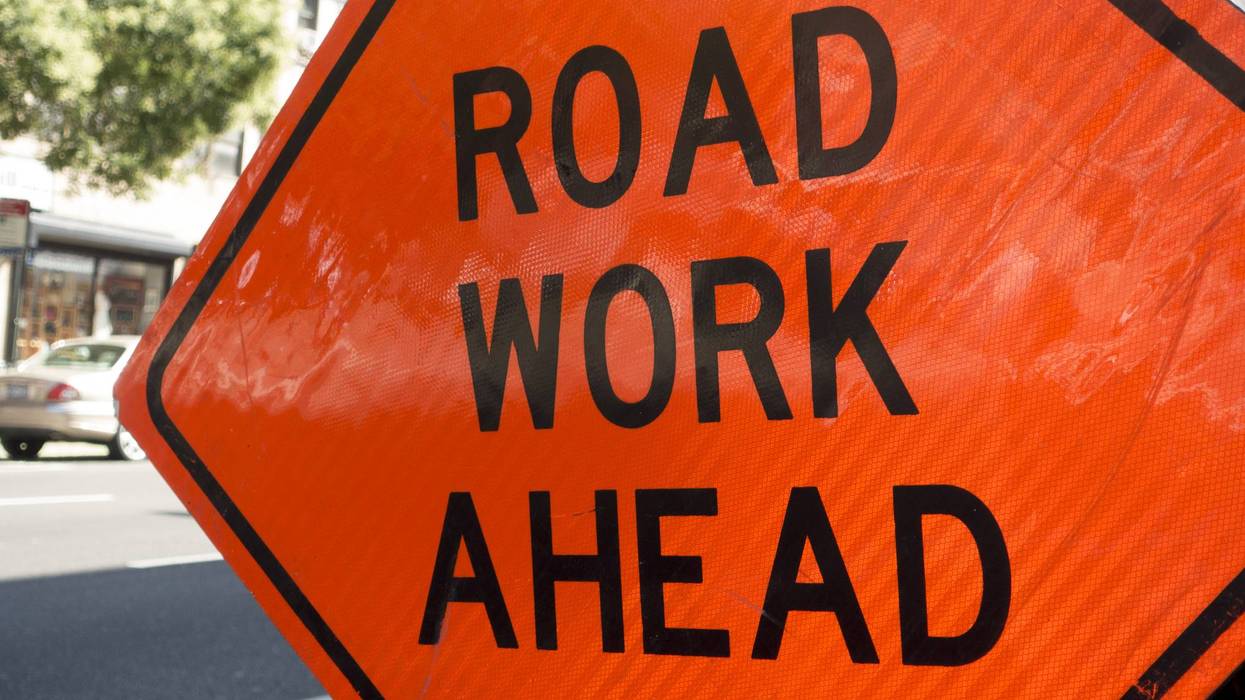 Orange diamond sign: "ROAD WORK AHEAD" on a sunny street.