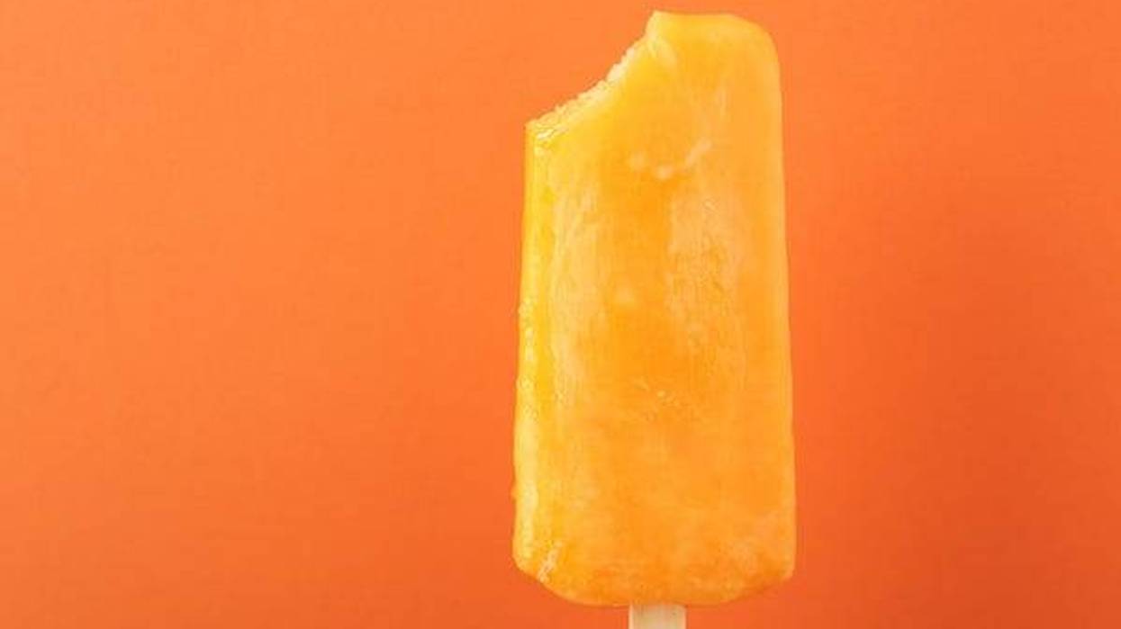 Orange popsicle with bite out of it against orange background