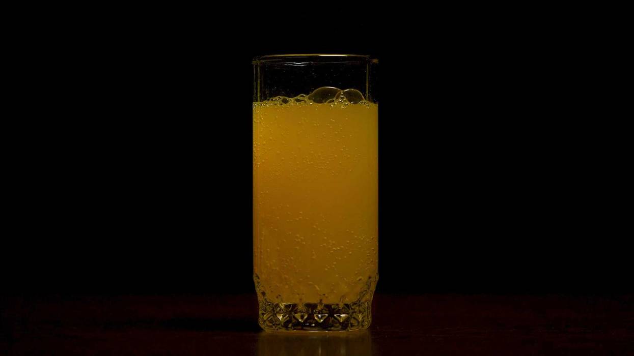 Orange soda large glass, overflowing glass of orange soda closeup with bubbles isolated on black background. Pouring Orange Drink. Slow Motion. Carbonated orange drink is poured into a glass. Pouring orange juice soda in glass in slow motion, black background