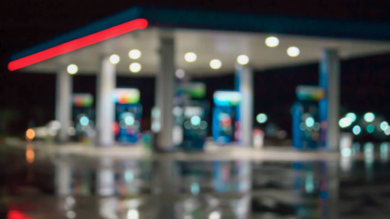 Out-of-focus gas station at night, bright lights illuminate pumps and reflect on wet ground.