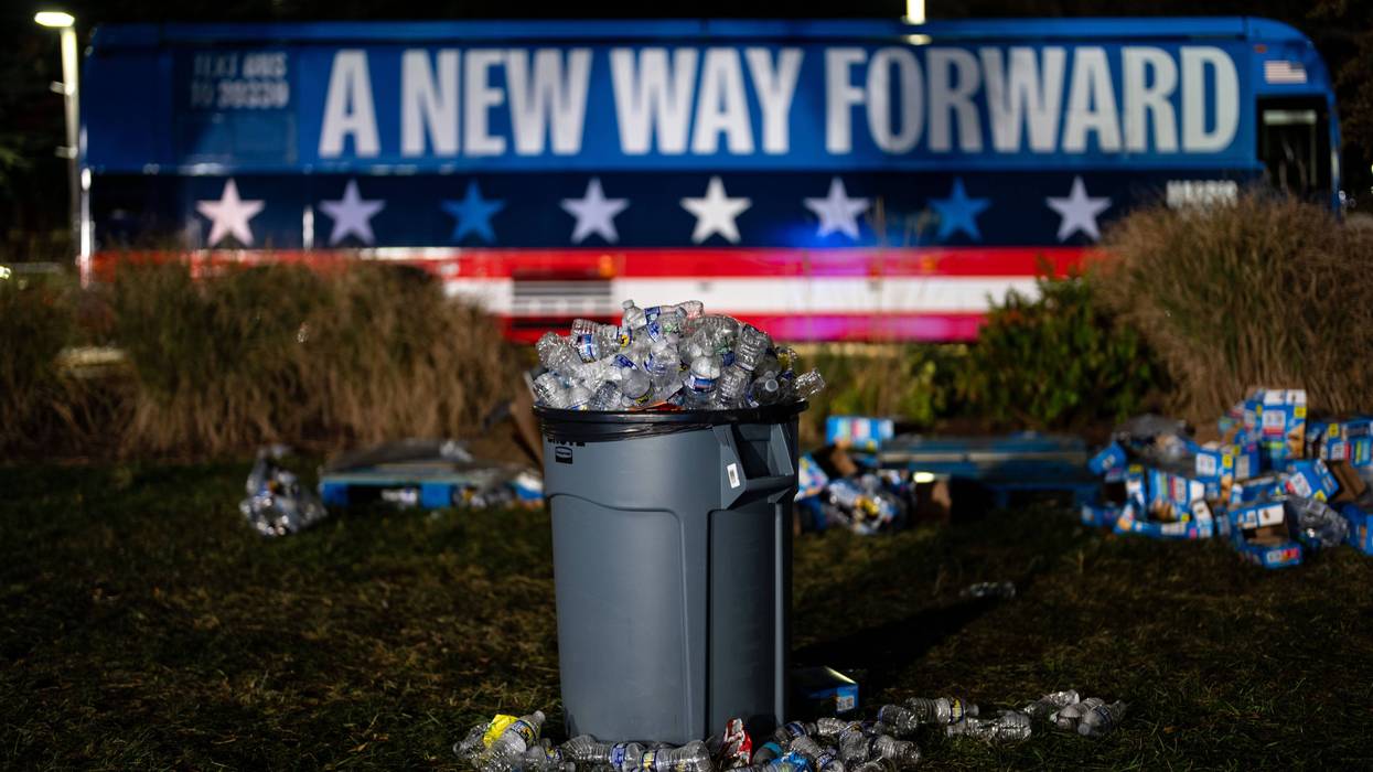 overflowing trash can with a campaign bus that says a new way forward in the background