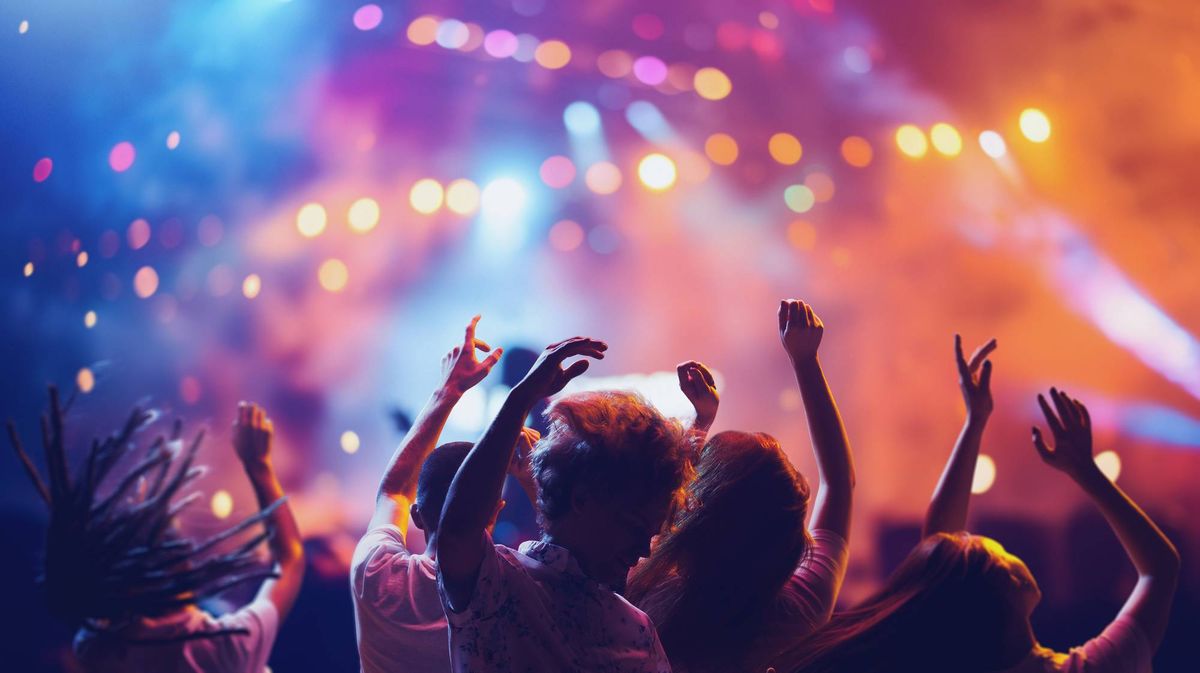 Overjoyed happy young people dancing, jumping and singing during concert of favorite group. Musical summer festival.