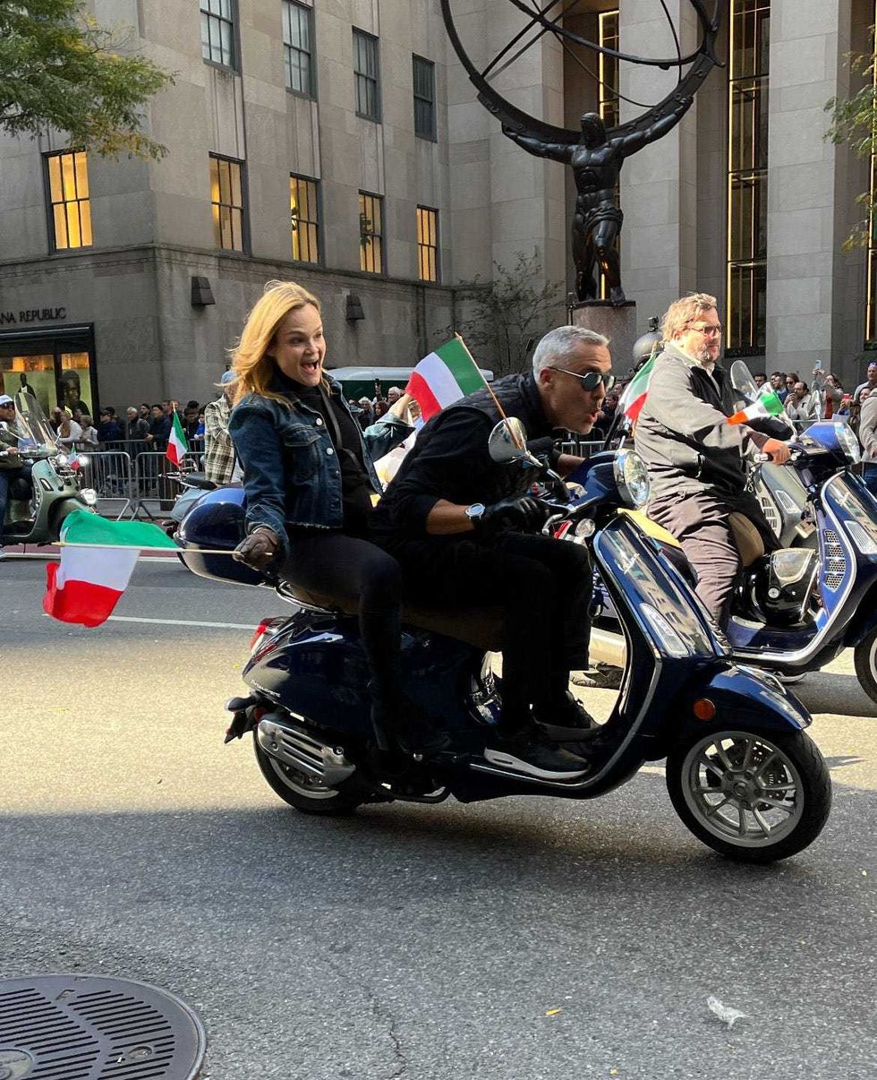 Parade participants ride Vespas and wave Italian flags