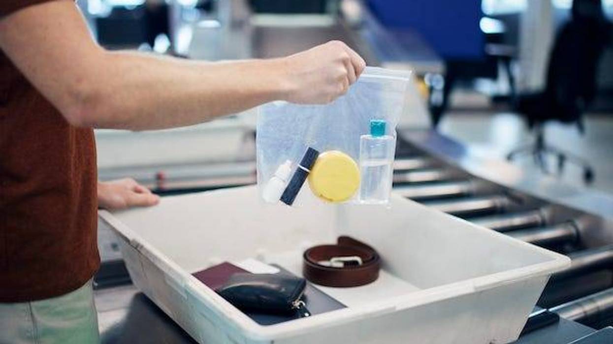 Passenger holding plastic bag with liquids above container with laptop and personal items