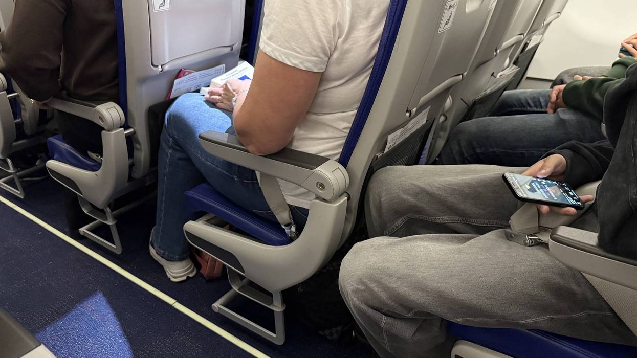 Passengers seated inside an airplane cabin with visible seat belts, legroom, and personal belongings during a commercial flight