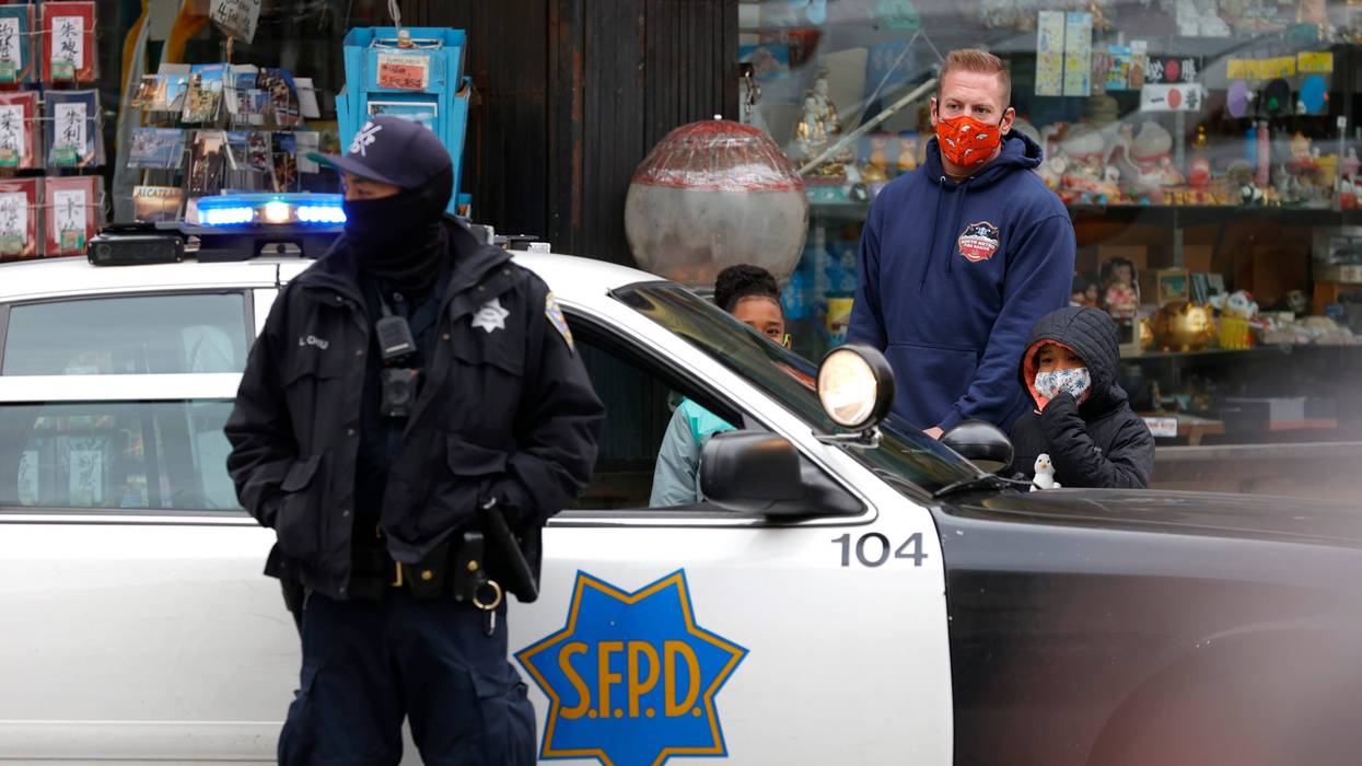 Pedestrians wait to cross the street as a San Francisco police officer stands guard on Grant Avenue in Chinatown on March 17, 2021 in San Francisco, California.