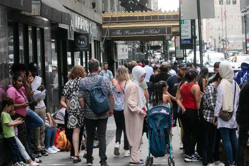 Pedestrians walk past migrants outside the Roosevelt Hotel, the city
