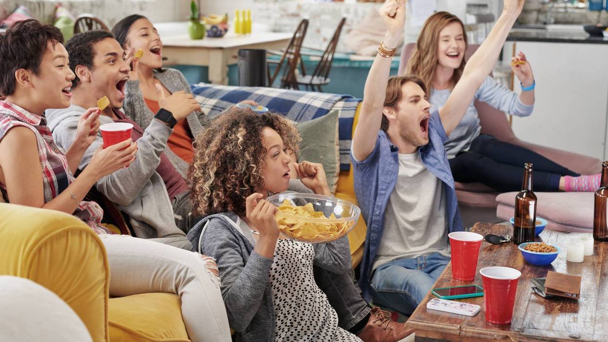 People gather around a couch to watch and cheer on a football game.