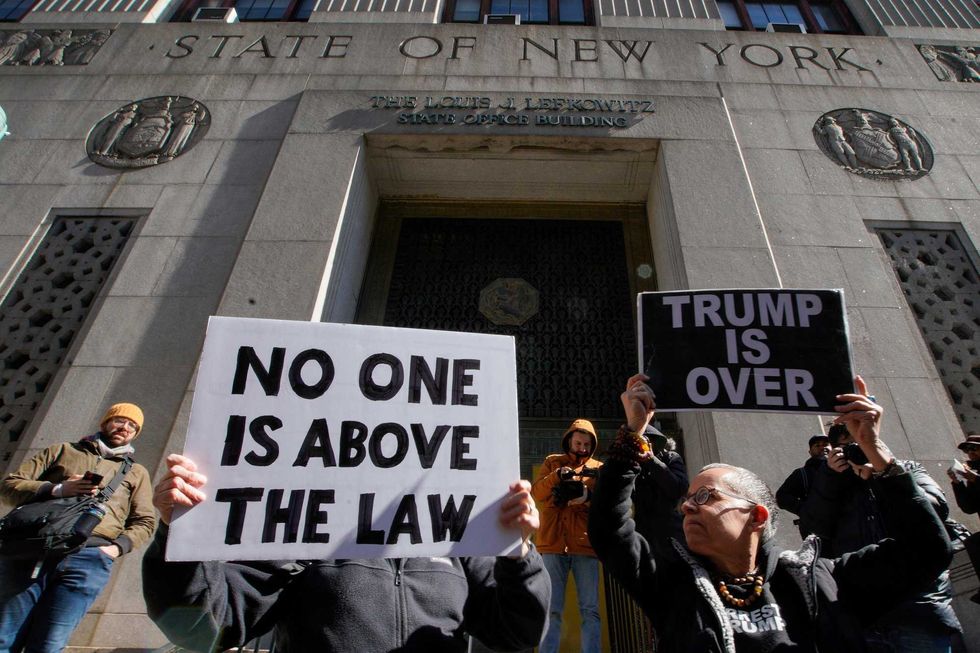 People hold up posters as part of a protest in front of the courthouse ahead of former President Donald Trump
