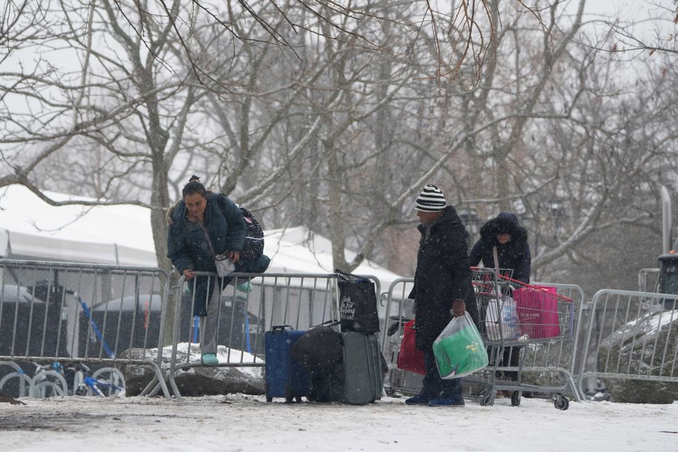 People hop a fence to get to a footbridge to Manhattan at a temporary shelter for migrants on Randall