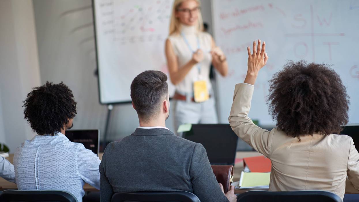 people in a meeting, one woman has her hand raised