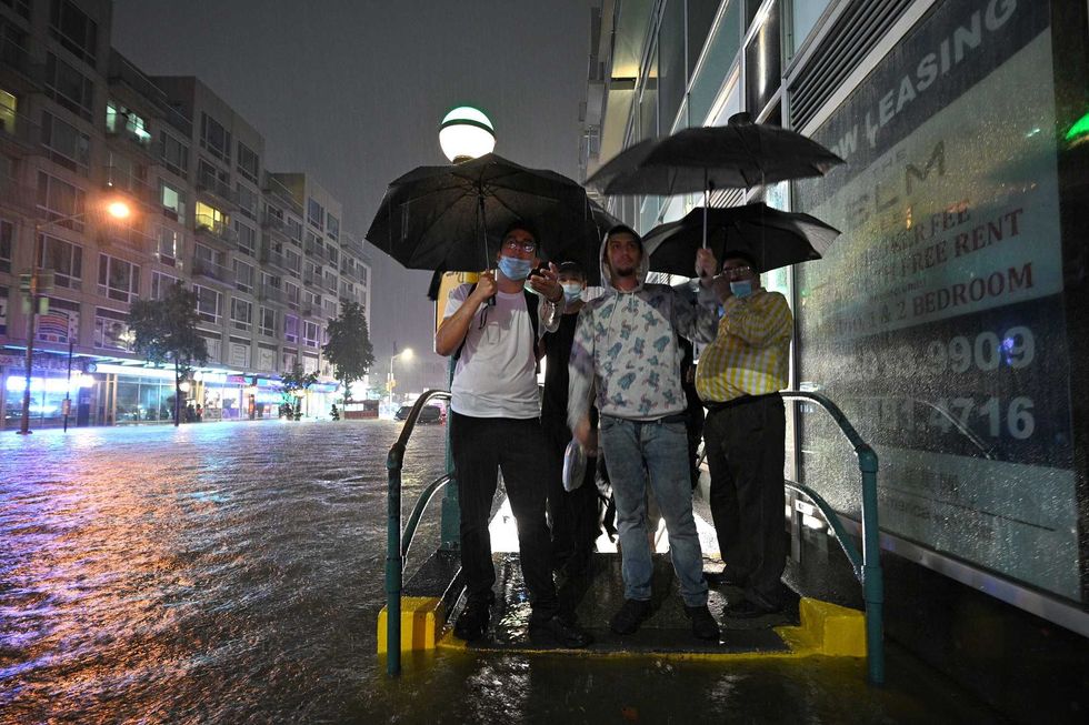 People stand at a subway entrance as they debate to wade through several inches of water caused flash flooding after remnants of storm Ida brought three inches of rain per hour across the city, in the New York City borough of Queens, NY, September 1, 2021