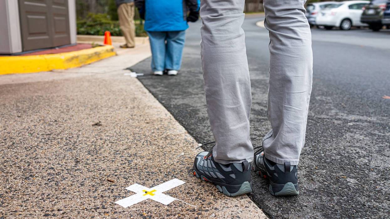People standing waiting in line far apart to maintain social distance distancing during covid-19 coronavirus outbreak with mark cross signs on sidewalk pavement by grocery food store shop shopping