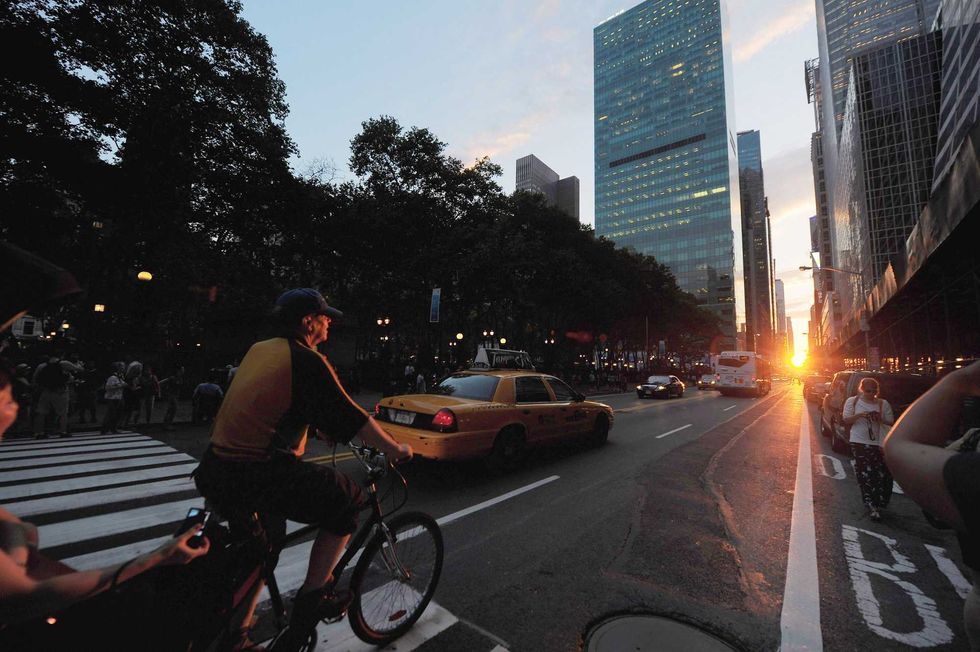People take photos and ride towards the setting sun during "Manhattanhenge" on July 13, 2011 in New York City. This semiannual occurrence was a half-sun Manhattanhenge, in which the setting sun aligns east-west with the street grid of the city.