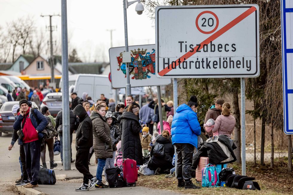 People wait with their belongings at the Tiszabecs-Tiszaujlak border crossing as they flee Ukraine on February 25, 2022 in Tiszabecs, Hungary