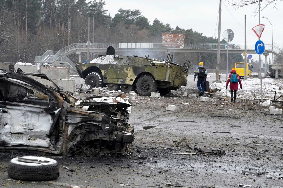 People walk by a damaged vehicle and an armored car at a checkpoint in Brovary, outside Kyiv, Ukraine, Tuesday, March 1, 2022