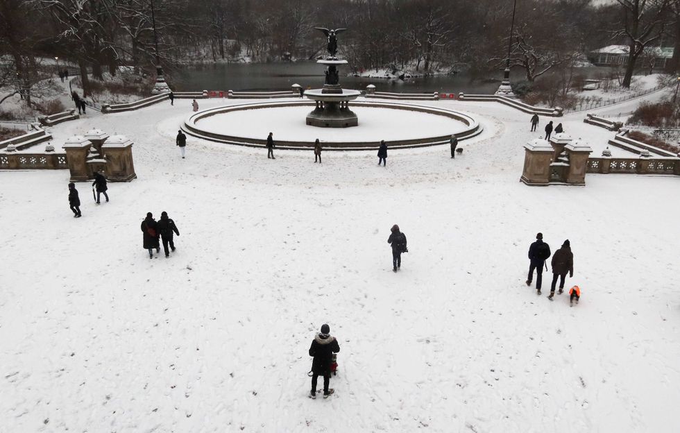 People walk by the Bethesda Fountain as snow falls in Central Park on January 16, 2024