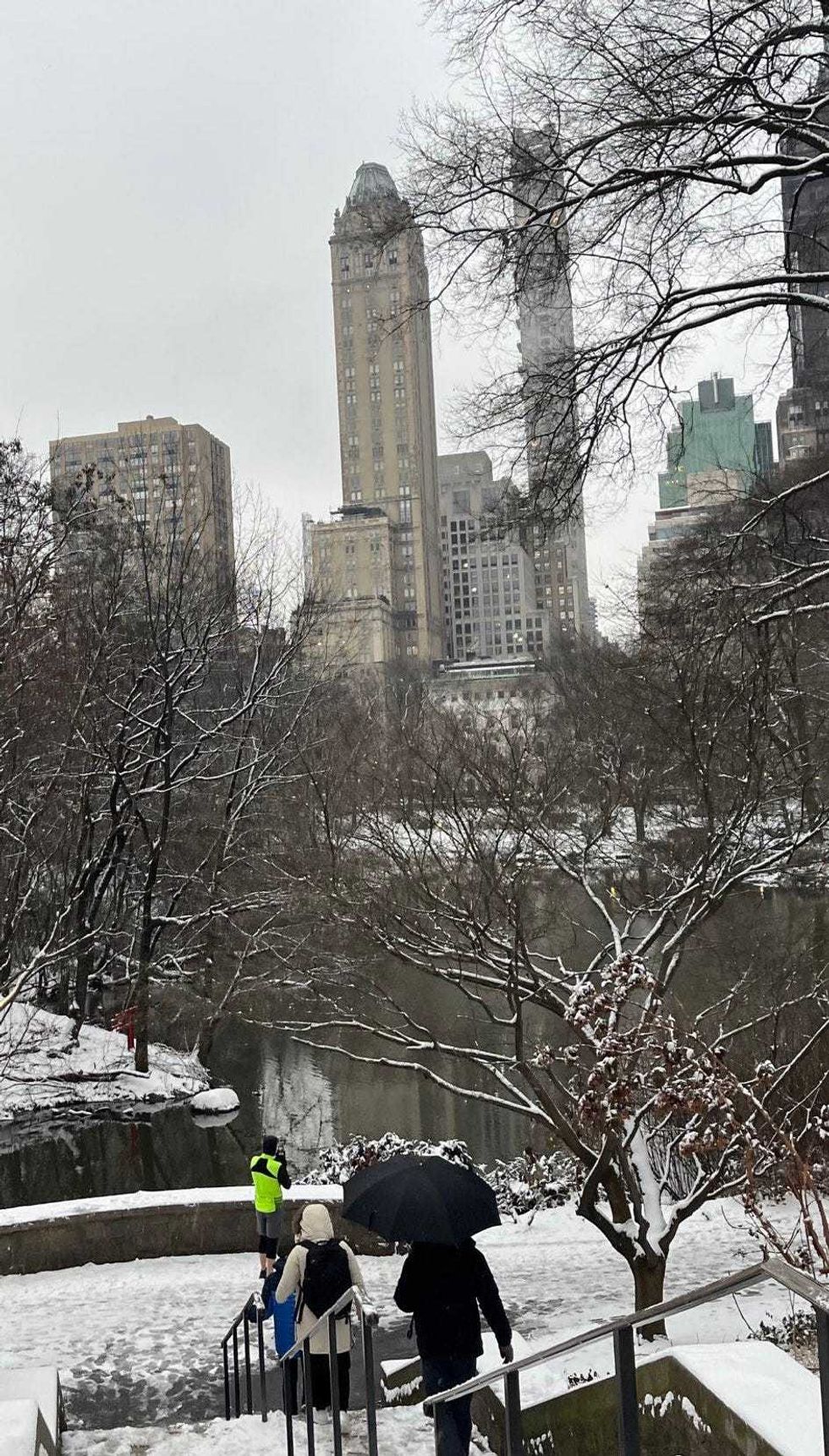 People walk in Central Park as snow falls on the city on January 16, 2024