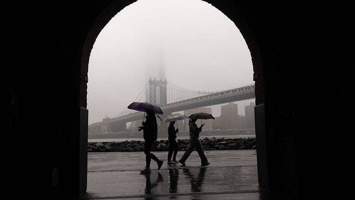 People walk in the rain across from a fog-covered Manhattan skyline on May 6, 2025 in New York City.