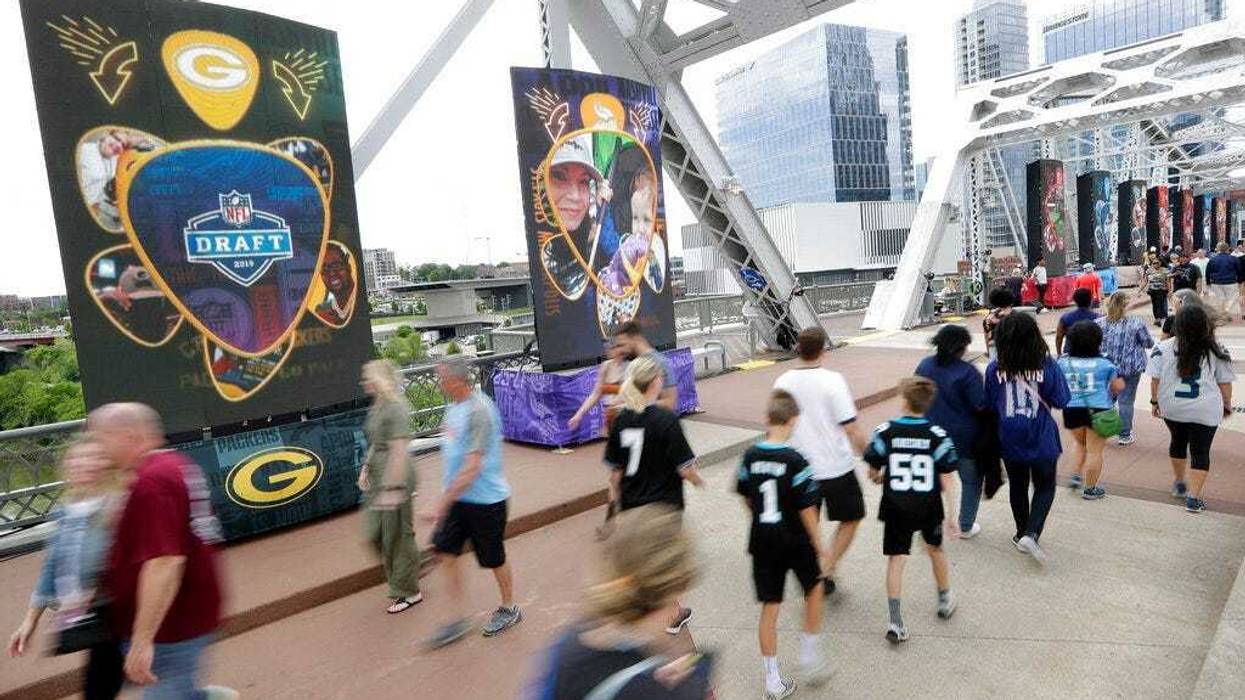 People walk on a bridge lined with video boards providing news on draft picks on the final day of the NFL football draft Saturday, April 27, 2019, in Nashville, Tenn. (