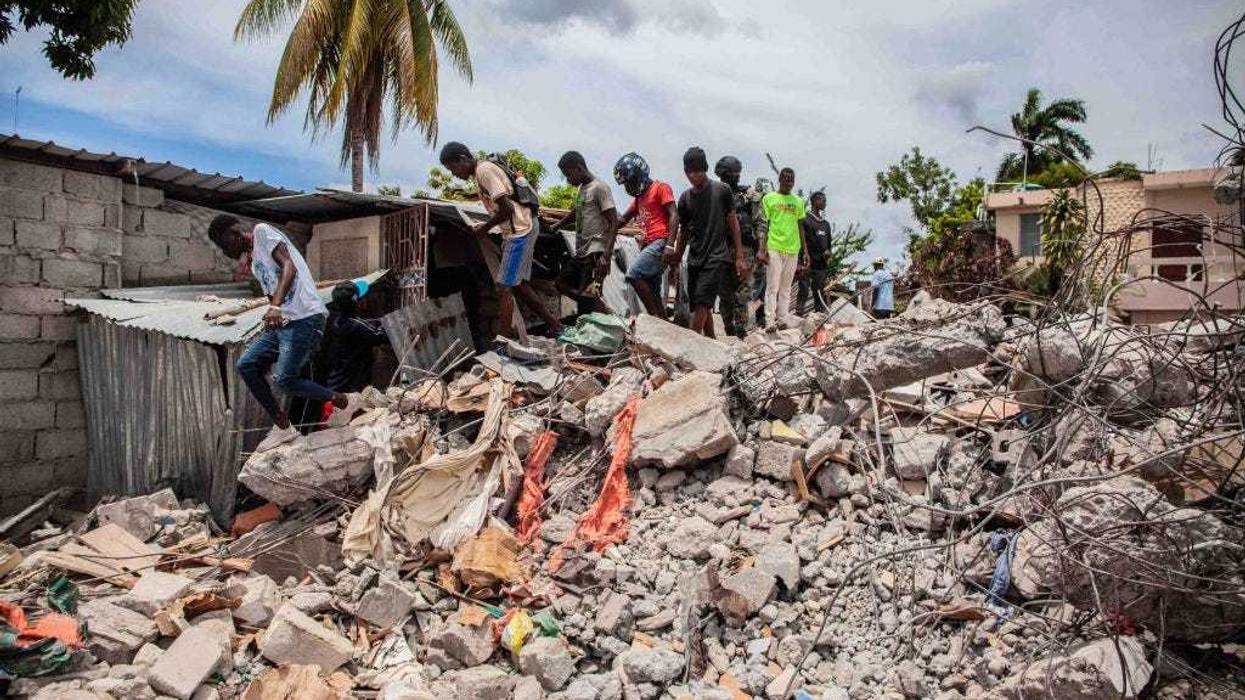People walk over a pile of rubble from a collapsed building after a 7.2-magnitude earthquake struck Haiti on August 16, 2021 in Les Cayes, Haiti.