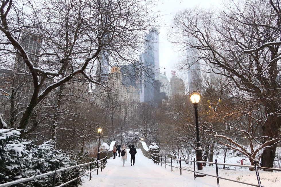 People walk over the Gapstow Bridge as snow falls in Central Park on January 16, 2024