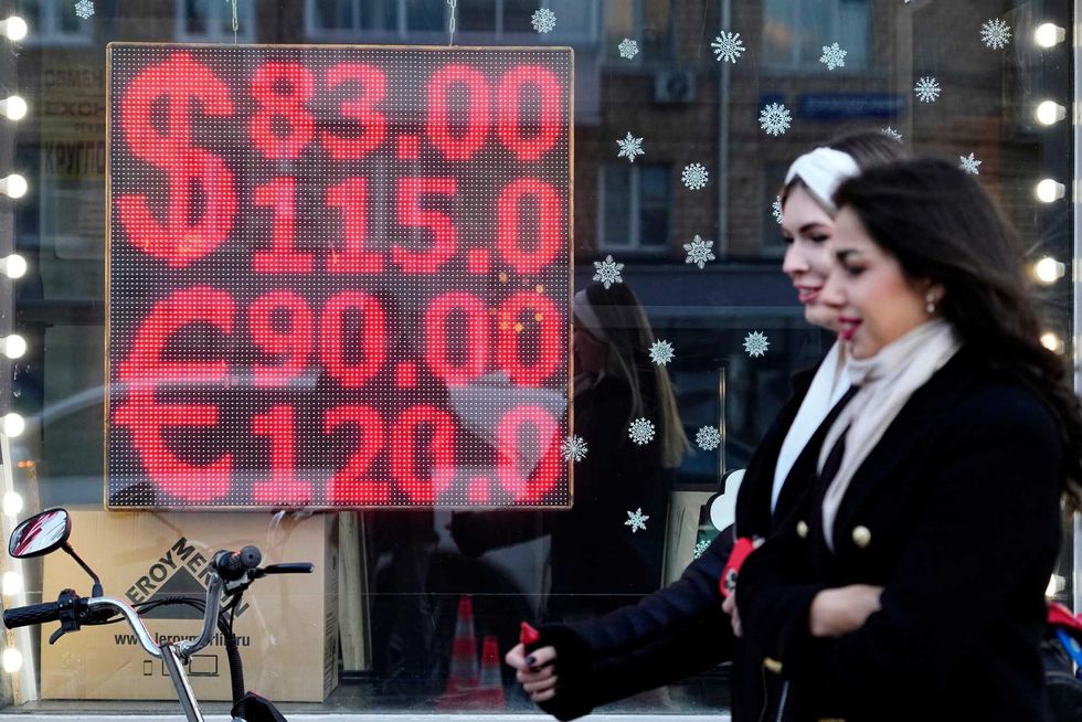 People walk past a currency exchange office screen displaying the exchange rates of U.S. Dollar and Euro to Russian Rubles in Moscow