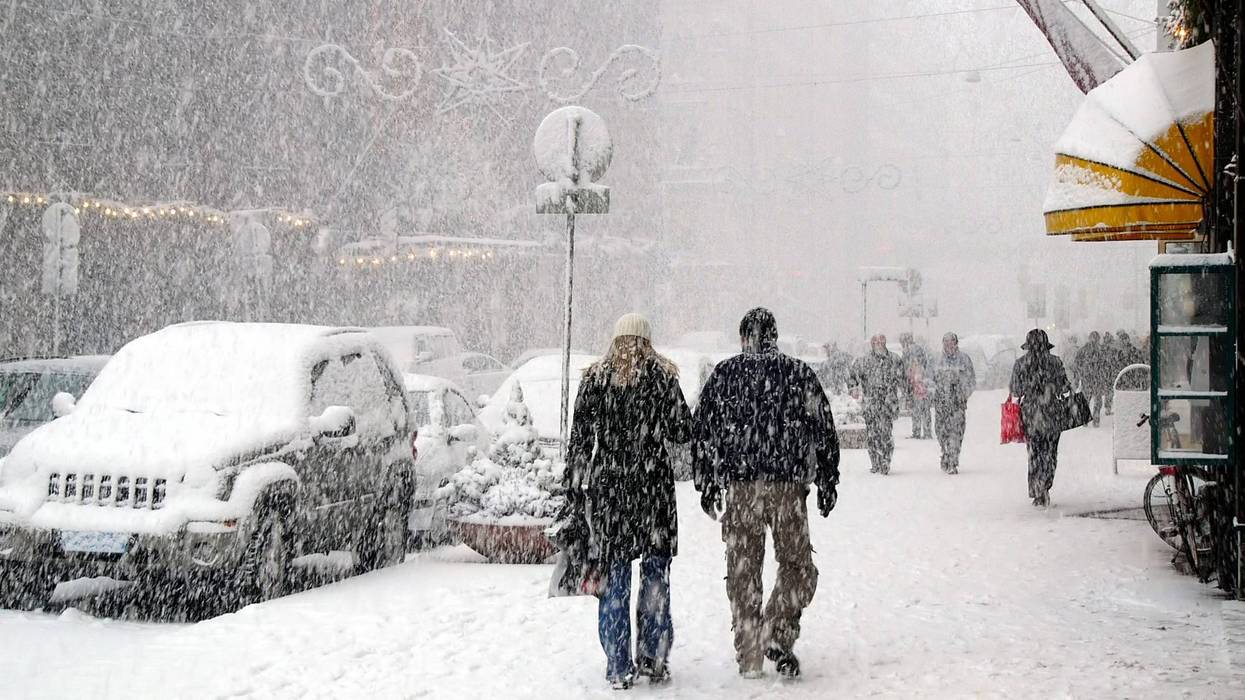 People walking down sidewalks in a snow storm in a city