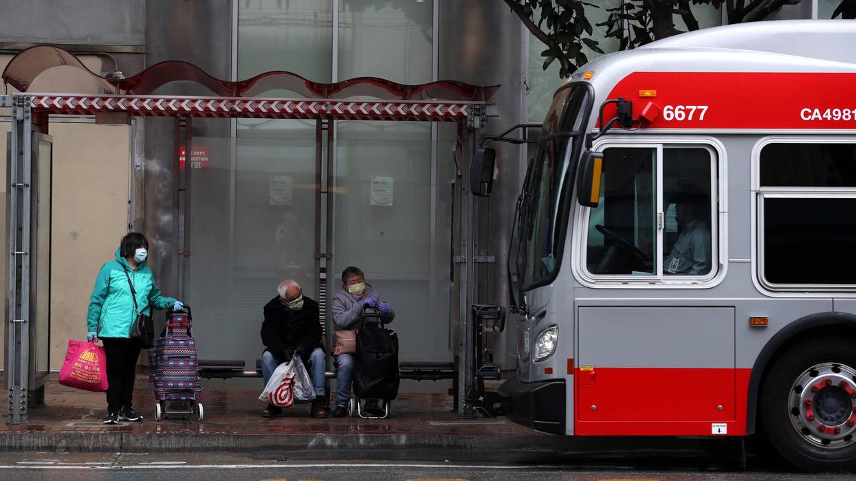 People wear masks as they wait in a bus shelter for a San Francisco MUNI bus during the coronavirus (COVID-19) pandemic on April 06, 2020 in San Francisco, California.