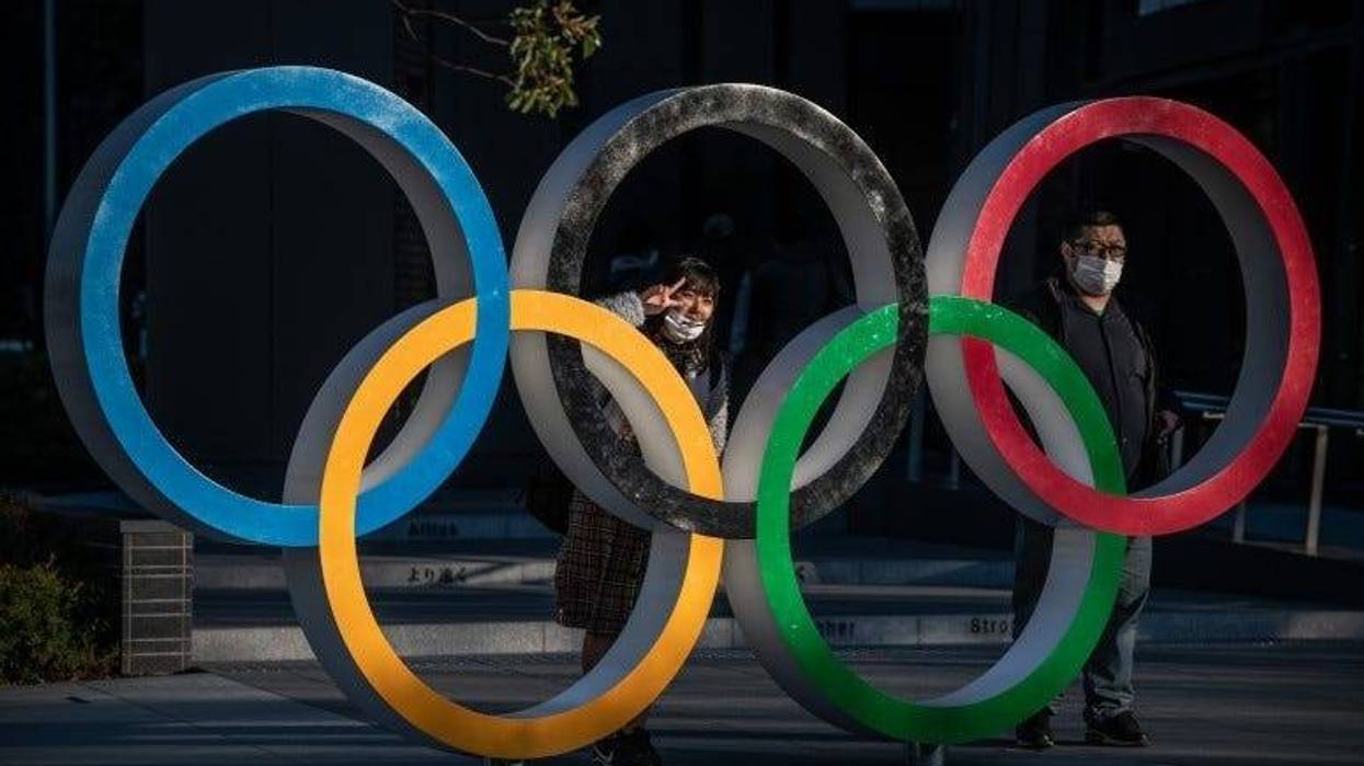 People wearing face masks pose for photographs next to Olympic Rings in Tokyo, Japan. The 2020 Olympic Games are postponed.