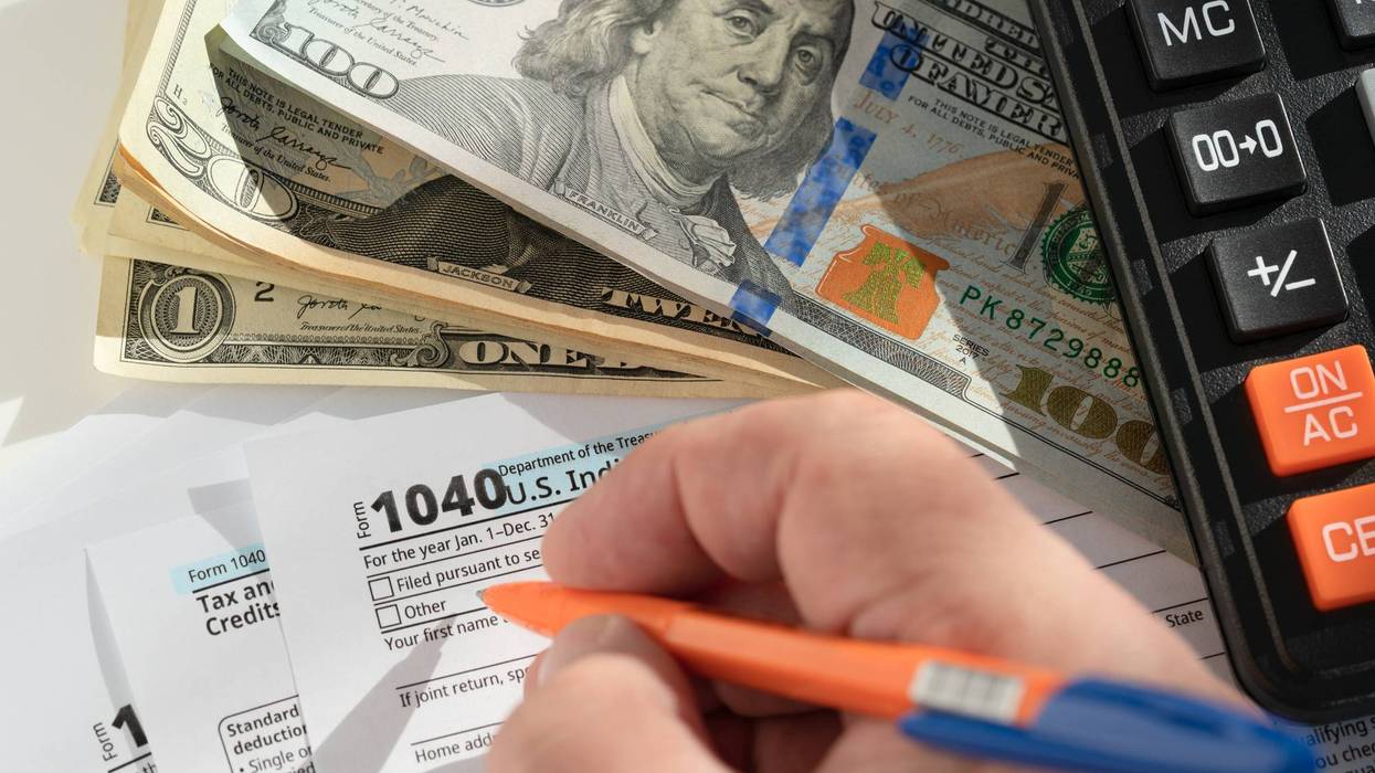 Person filling out US 1040 tax form with cash and calculator