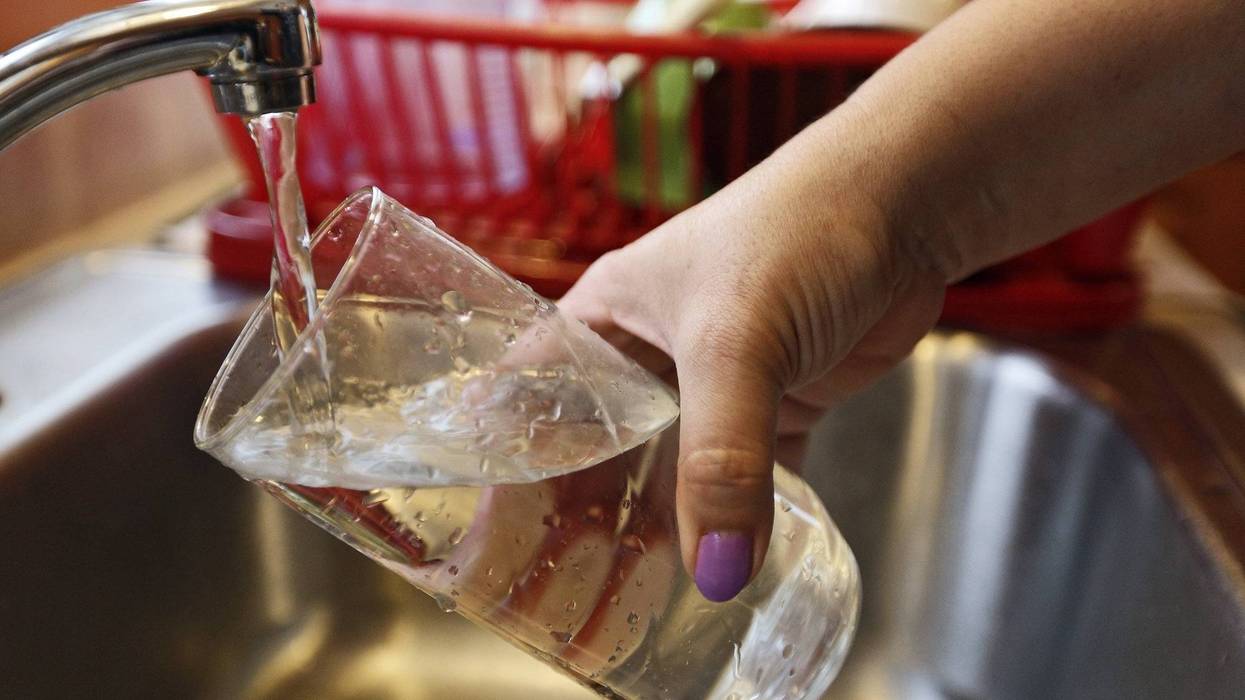 person fills glass of water from kitchen faucet