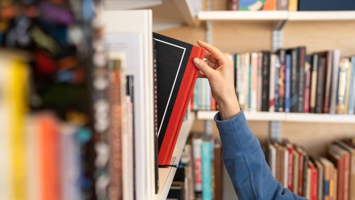 person grabbing a book from a library book shelf
