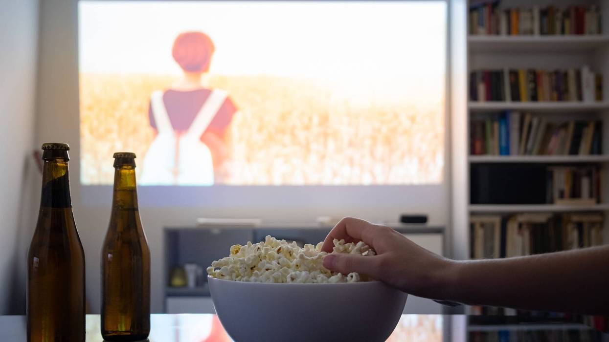 person grabbing popcorn out of a bowl with movie projected on wall at home