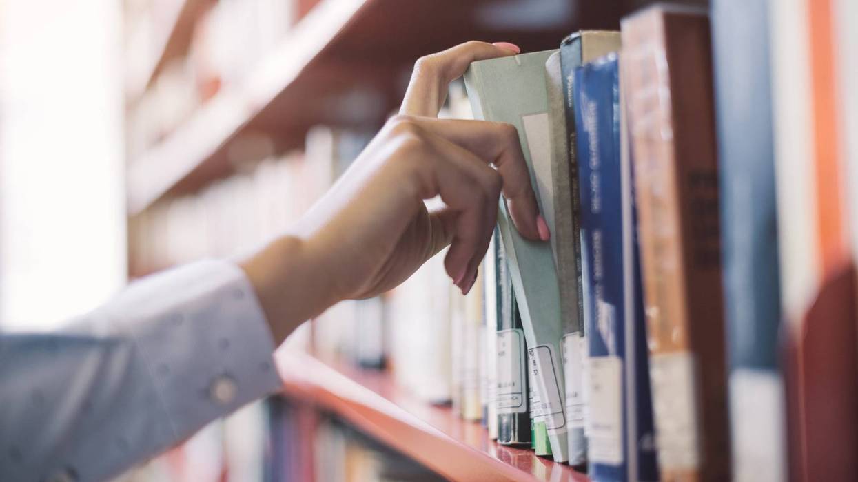 person pulls a book from a library shelf