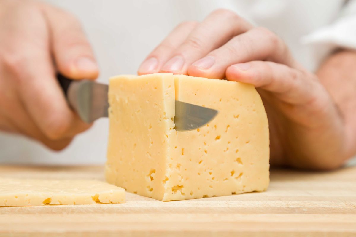 Person slicing a block of cheese.