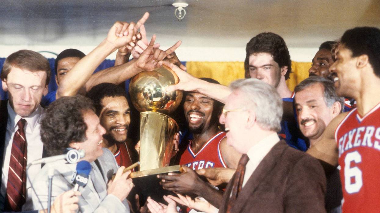 Philadelphia 76ers Maurice Cheeks (L) and Andrew Toney (R) victorious, holding Walter A. Brown trophy with teammates in locker room after winning game and series at The Forum. Game 4.