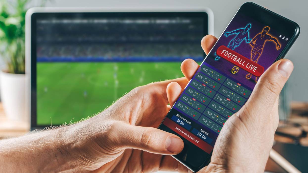 phone in foreground that shows football bets, football game on tv in background
