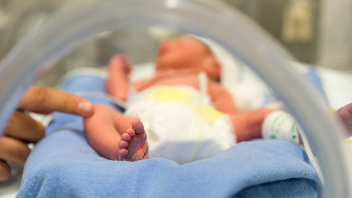 Photo of a premature baby in incubator. Focus is on his feet and toes. The doctor is touching him to check his reflexes. There are cables and tubes in the out-of-focus area.