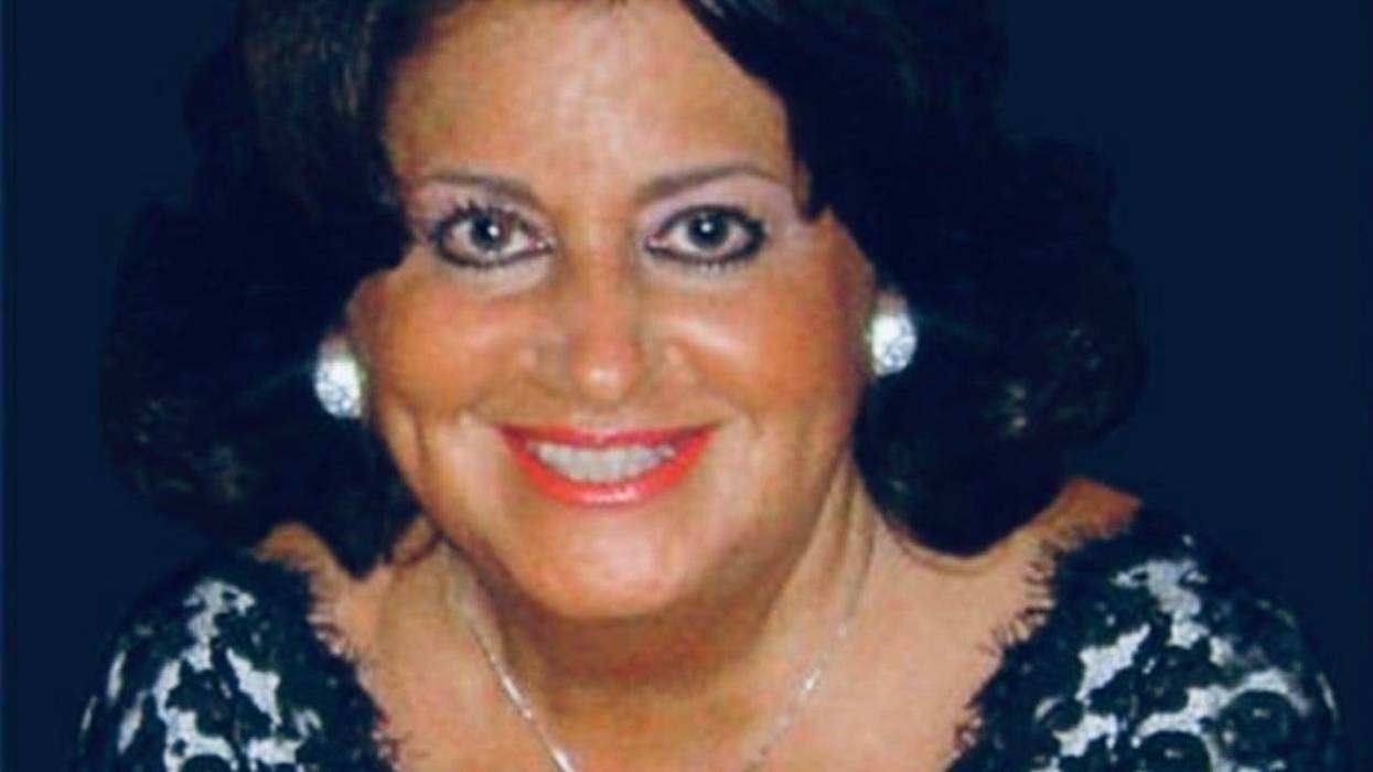Photo of older woman with tan skin, makeup and jewelry in black lace dress smiling