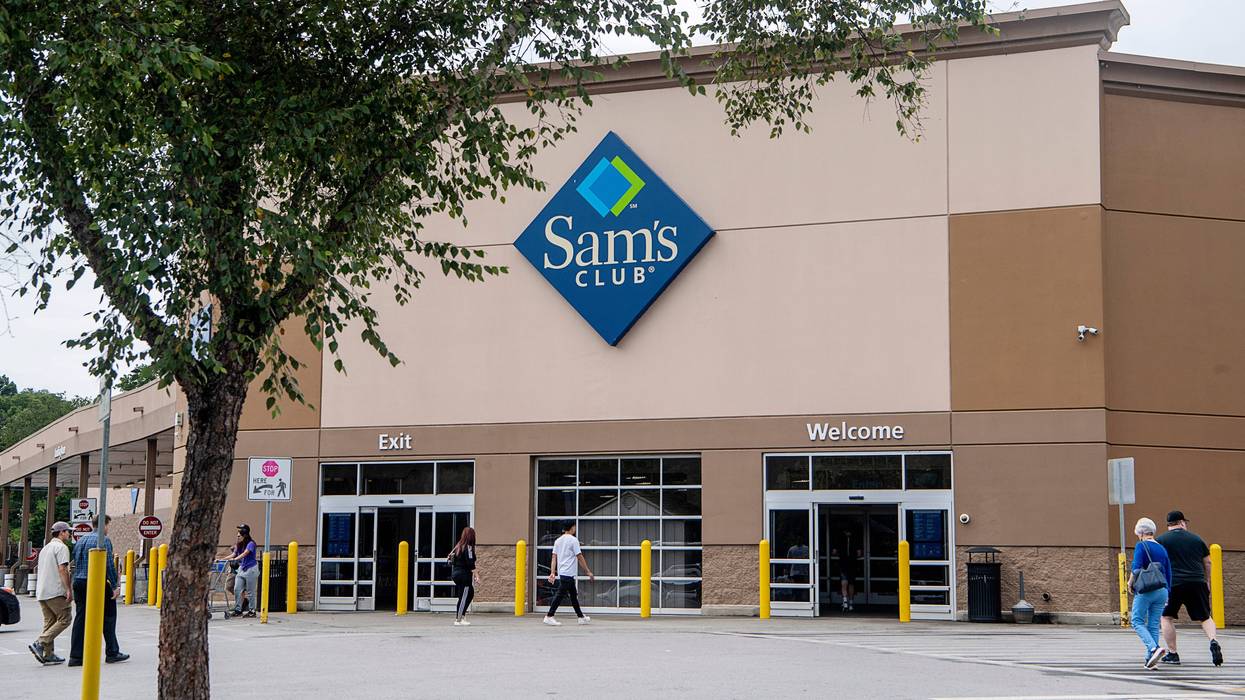 Photo of the front exterior of Sam's Club big box store with customers walking inside. A tree is in the foreground.