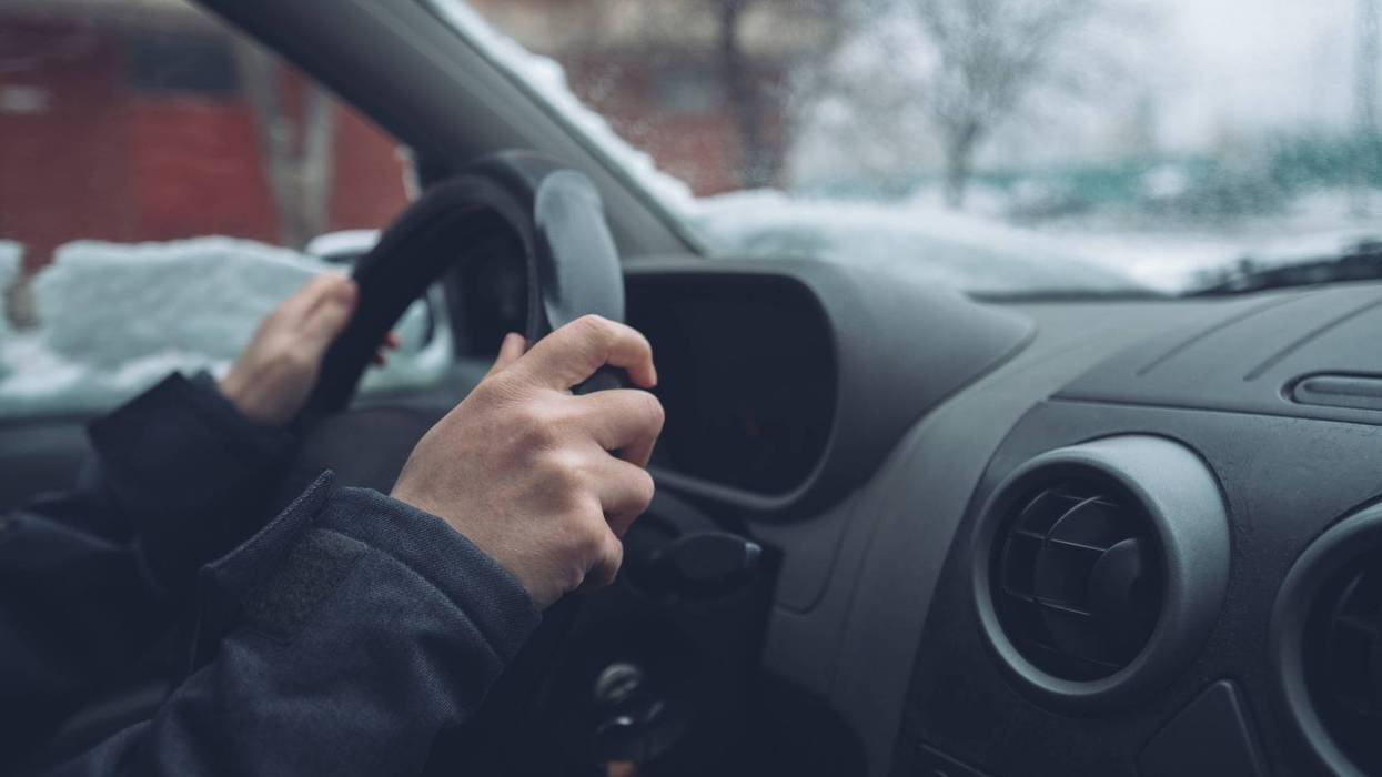 Photograph of a driver's hands on the steering wheel of a car, with snow on the windshield