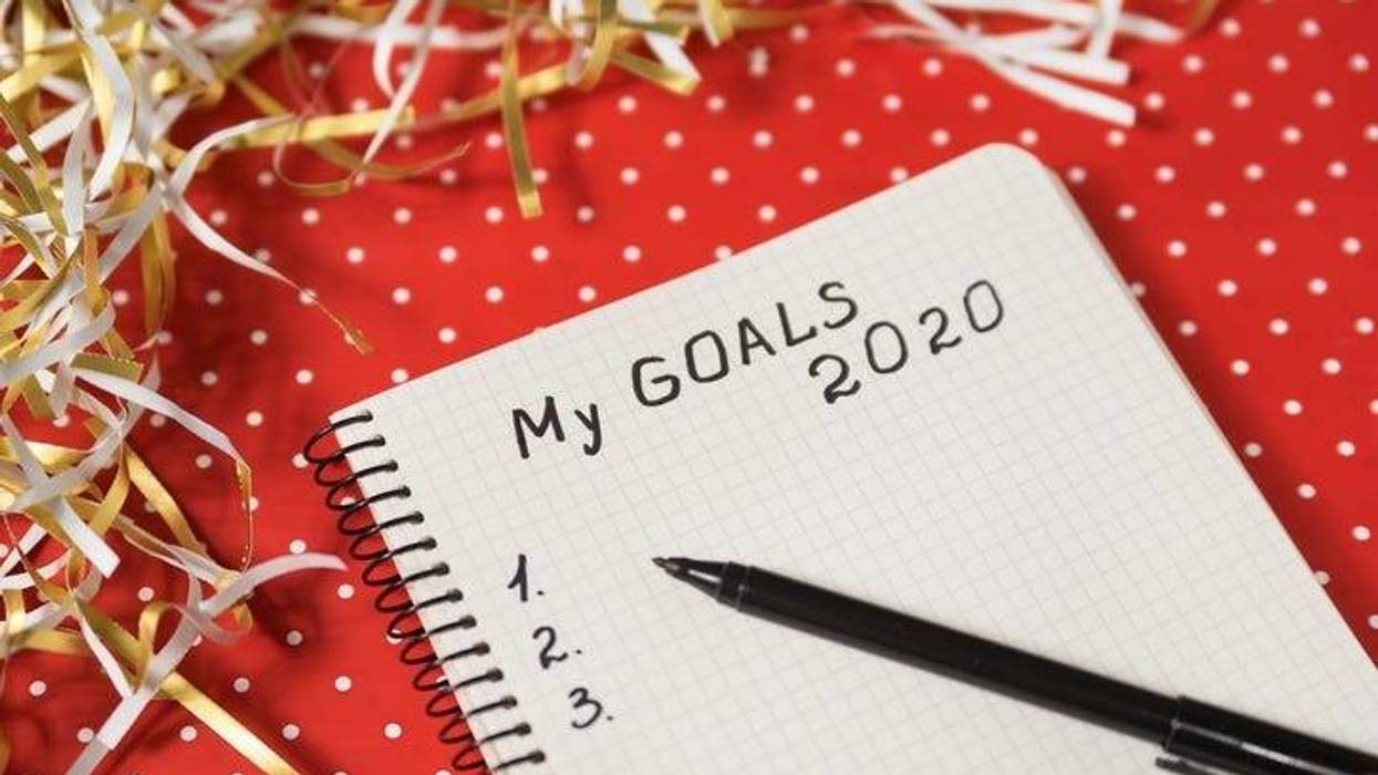 Phrase My Goals 2020 in a notebook, black pen. Red background and tinsel. New Years concept