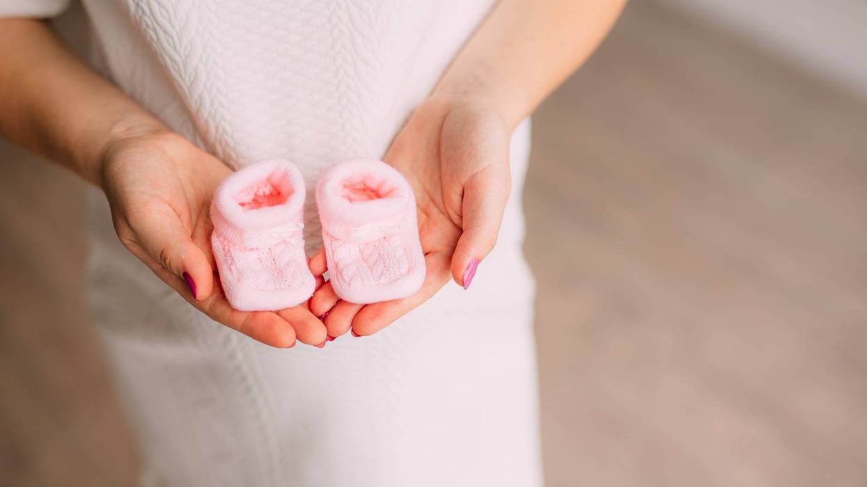 Pink baby booties in the hands of a pregnant mother.