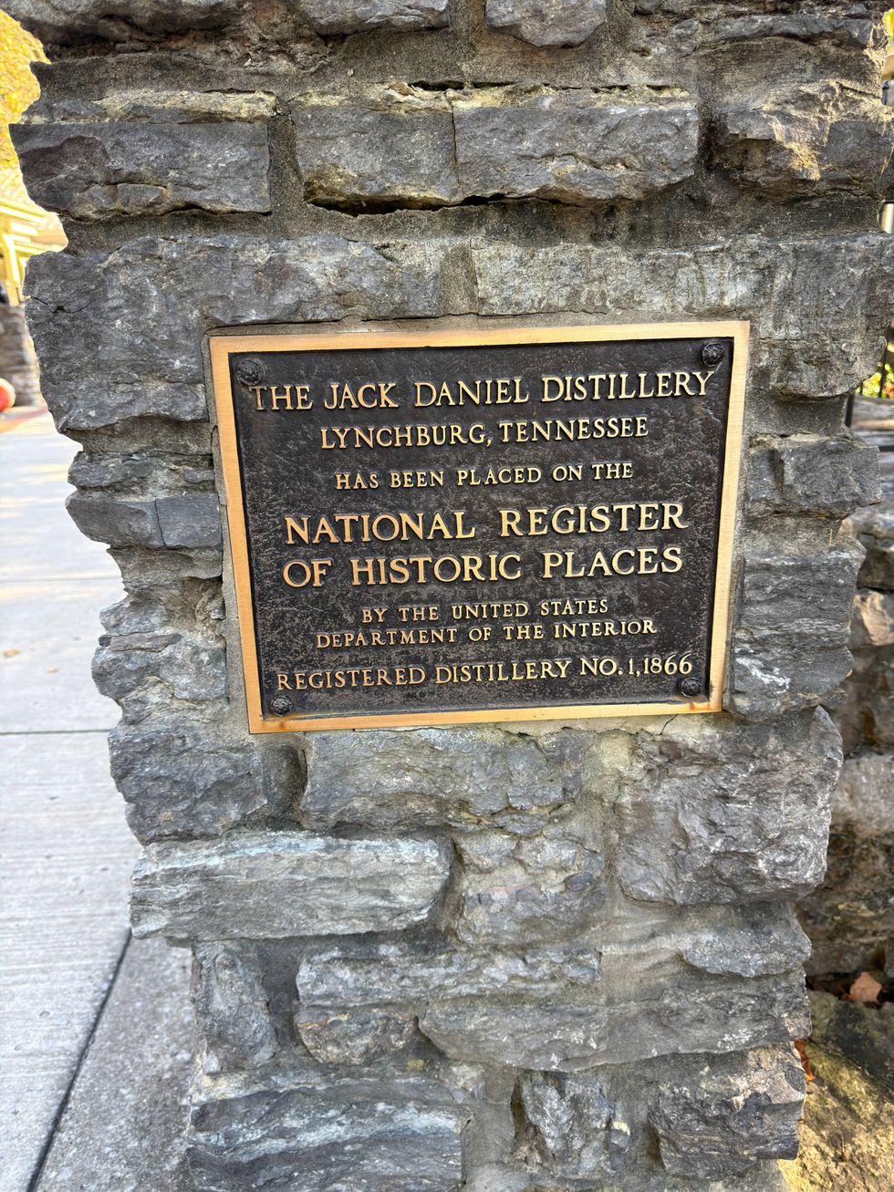 Plaque on a stone wall reads: "The Jack Daniel Distillery, Lynchburg, Tennessee has been placed on the National Register of Historic Places." Historic, official.