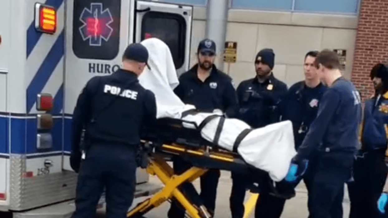 Police and paramedics loading a covered body on a stretcher into an ambulance.